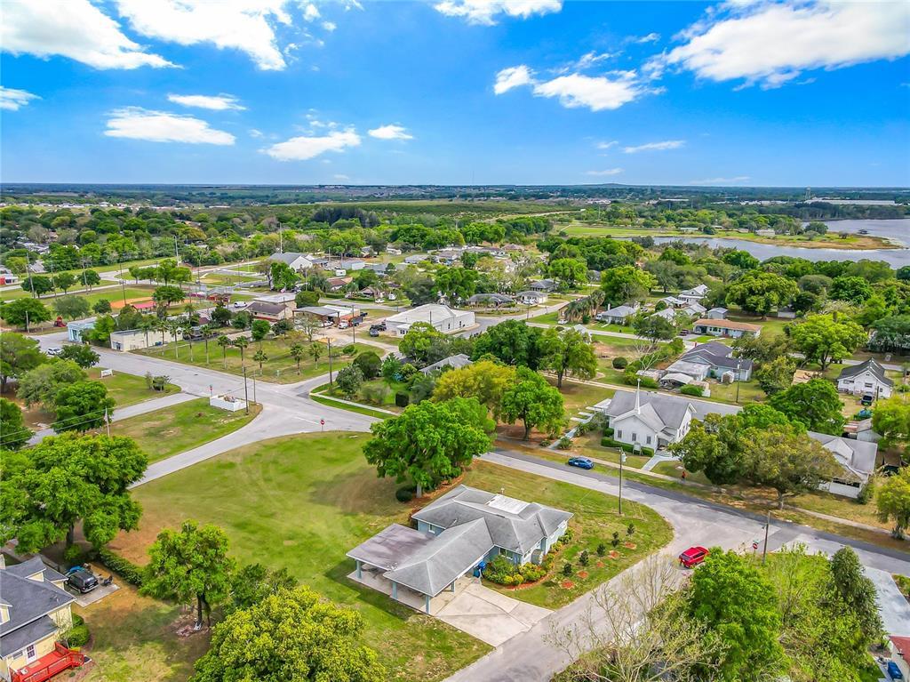 Aerial view of a suburban landscape with houses, well-manicured lawns showcasing expert lawn care, trees, and intersecting roads under a partly cloudy sky.